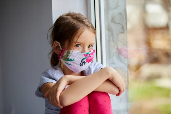 Meisje, kind met masker zit op ramen, coronavirus quarantaine — Stockfoto