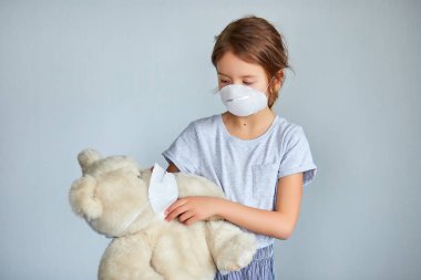 Maskeli oyuncak ayıyı kucağına alan küçük bir kız. Coronavirus, covid-19 ve kirlilik koruma konsepti. Evde kal..