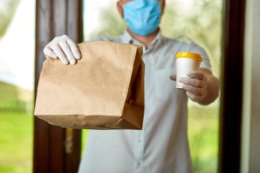 Kurye, koruyucu maskeli kurye ve tıbbi eldivenli teslimatçı paket yemek getiriyor. Karantina altında teslimat hizmeti, hastalık salgını, koronavirüs covid-19 salgını. Evde kal, güvenli konsept.