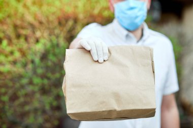 Kurye, tıbbi lateks eldivenli kurye Coronavirus salgını sırasında, COVID-19 'da kahverengi kese kağıtlarıyla çevrimiçi alışveriş yapıyor. Evde kal, güvenli konsept..