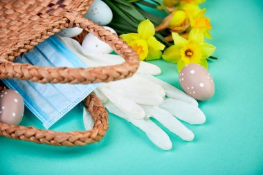 Coronavirus karantinasında paskalya kompozisyonu, koruyucu tıbbi maske ve eldivenlerin yanındaki sepette yumurta ve narsis çiçekleri, Coronavirüs salgınından dolayı Paskalya tatili konsepti