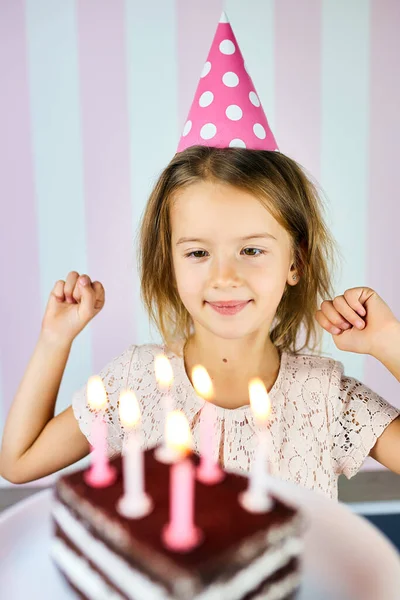 小さなブロンドの女の子が誕生日ピンクの帽子 キャンドル付きのチョコレートの誕生日ケーキで笑っています 子供は誕生日を祝う 誕生日おめでとう — ストック写真