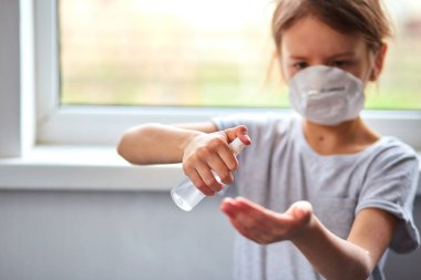 Küçük kız hijyenik maske takıyor ve korumak için alkol spreyi sıkıyor. Coronavirus, covid-19 ve kirlilik koruma konsepti. Evde kal..