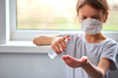 Küçük kız hijyenik maske takıyor ve korumak için alkol spreyi sıkıyor. Coronavirus, covid-19 ve kirlilik koruma konsepti. Evde kal..