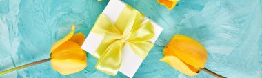Sarı lalenin yanında sarı kurdeleli beyaz hediye kutusu mavi arka planda. Düz yatıyordu. Anneler Günü. Tebrik kartı. Uzayı kopyala Bahar.
