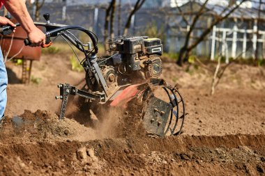 Bahçede Garden Tiller 'la çalışan bir adam. Bahçe dümeni çalışıyor, kapatın. Baharda traktör tarlası olan bir adam. Modern tarım, teknoloji tarımı.