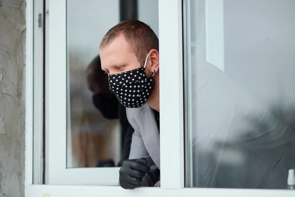 Man in black mask and medicine gloves looking from window, coronavirus quarantine, work from home. Stay at home. Concept of coronavirus quarantine. MERS-Cov. Novel coronavirus.