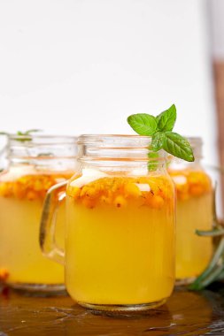 Virüs koruma içeceği, koronavirüs, bağışıklık konsepti. Vitaminik sağlıklı deniz dikenli çay küçük cam bardaklarda taze çiğ deniz dikenli böğürtlen, siyah arka planda bal bağışıklık sistemi destekleyici gıda, antiviral içecek..