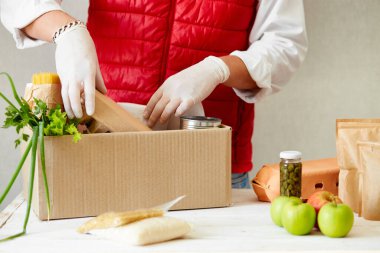 Koruyucu tıbbi maske ve eldiven giyen gönüllü bağış kutusuna yiyecek koyuyor. Kırmızı yelekli, yüz maskeli ve yiyecek dolu eldiven kutulu bir teslimatçı. Hizmet karantina salgını Coronavirüs gribi virüsü 2019-ncov konsepti