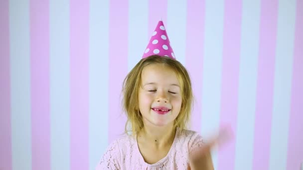 Маленька блондинка в очікуванні сюрпризу, посміхається в день народження рожева шапка — стокове відео