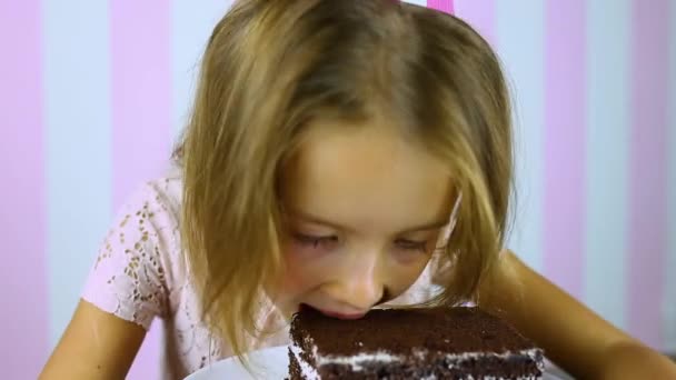 Feliz y sonriente niña en rosa tapa comer pastel de chocolate de cumpleaños — Vídeos de Stock