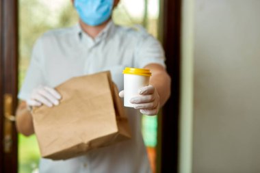 Kurye, koruyucu maskeli kurye ve tıbbi eldivenli teslimatçı paket yemek getiriyor. Karantina altında teslimat hizmeti, hastalık salgını, koronavirüs covid-19 salgını. Evde kal, güvenli konsept..