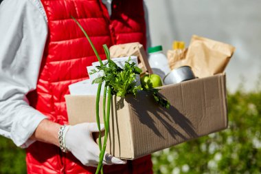 Koruyucu maskeli ve tıbbi eldivenli kurye yemek kutusu getiriyor. Virüs salgını, koronavirüs paniği ve salgınlar sırasında eve yemek getirmek. Kendine dikkat et. Adam bağış kutusunu yiyecekle birlikte tutuyor.