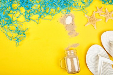 Deniz kabukları, beyaz parmak arası terlikler, sarı arka plan manzaralı kumlu cam. Yaz tatili planlamak, Coronavirus salgını, seyahat ve tatil planlarını değiştirmek. Düz yatıyordu.