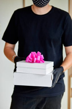 Korunaklı tıbbi maskeli, eldivenli, kuryeli adam temassız teslimat hediyeleri, bir koronavirüs salgını sırasında hediye kutusu. Evde kal, online alışveriş yap. Teslimat servisi karantina altında.
