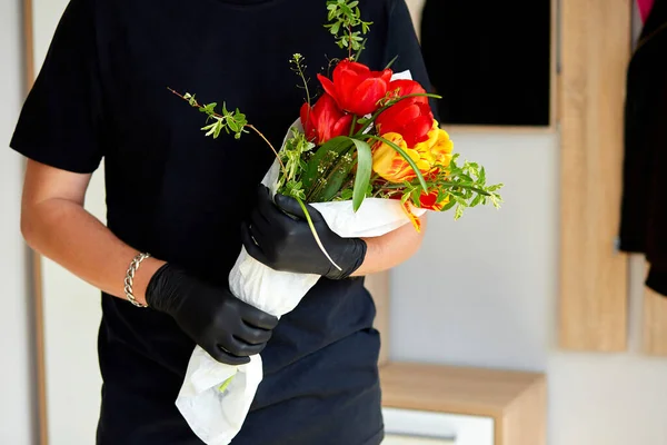 Courier, delivery man in black medical latex gloves safely delivers online purchases a bouquet of flower during coronavirus epidemic. Stay home, safe concept. Contactless delivery service under quarantine.