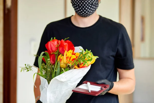 Courier, delivery man in black medical latex gloves safely delivers online purchases a bouquet of flower during coronavirus epidemic. Stay home, safe concept. Contactless delivery service under quarantine.