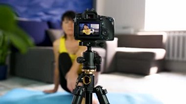 Spor kıyafetleri video blogunda zayıf vücut yapısı olan blogger son sınıf öğrencisi kadın evde yoga minderinde poz veriyor. Spor blogu, online eğitim. Coronavirus karantinası, evde kalın..