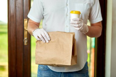 Kurye, koruyucu maskeli kurye ve tıbbi eldivenli teslimatçı paket yemek getiriyor. Karantina altında teslimat hizmeti, hastalık salgını, koronavirüs covid-19 salgını. Evde kal, güvenli konsept.