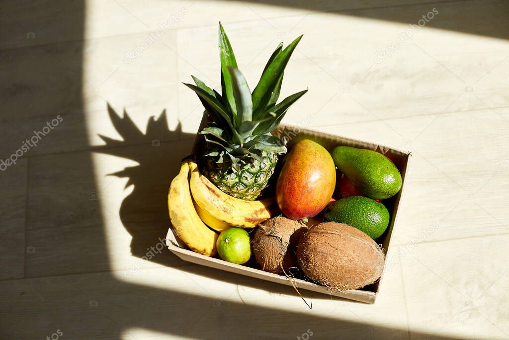 Assortment of organic exotic fruits in box, sunlight. Grocery bag with exotic fruits in front door, contactless delivery. Service quarantine pandemic coronavirus.