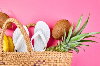 Beyaz terliklerin düz yatağı hasır bambu çanta ve pembe arka plan, üst manzara, fotokopi alanı üzerinde taze egzotik meyveler. Yaz plajı tatili konsepti. Boşluğu kopyala.