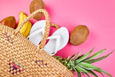 Beyaz terliklerin düz yatağı hasır bambu çanta ve pembe arka plan, üst manzara, fotokopi alanı üzerinde taze egzotik meyveler. Yaz plajı tatili konsepti. Boşluğu kopyala.