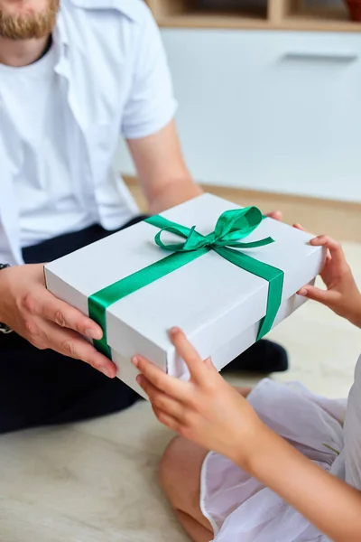 Little girl is giving her handsome father a gift box on Father\'s day, smiling daughter congratulating dad and giving present on birthday at home. I love you, dad. Happy Father\'s Day.