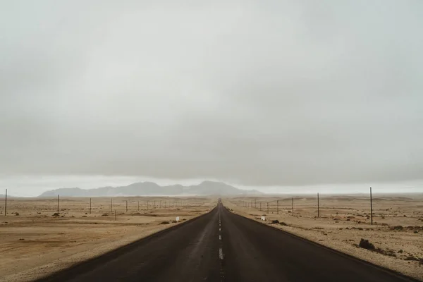 Villamos oszlopok száraz sivatagi hegyekben, drámai égbolttal — Stock Fotó