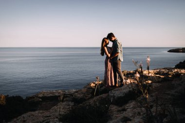 Çift silueti deniz kenarında romantik gün batımının keyfini çıkarıyor.