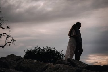Çiftler dağın tepesinde el ele tutuşup gün batımını izliyorlar.
