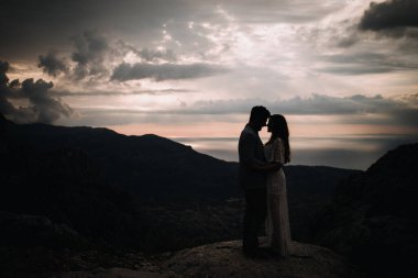 Çiftler dağın tepesinde el ele tutuşup gün batımını izliyorlar.