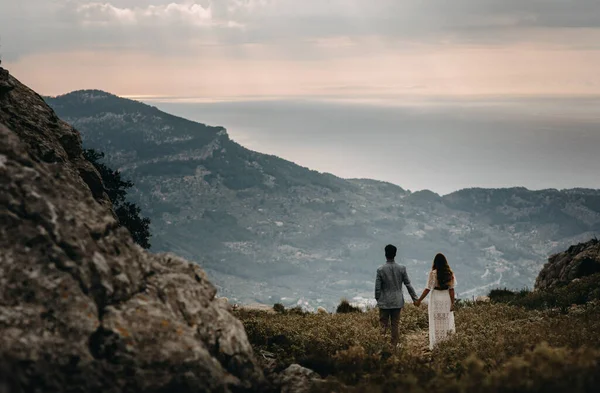 stock image couple standing on the top of mountain, holding hands and watching sunset