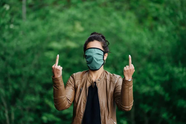 Foto de uma mulher levantando o dedo médio usando uma máscara facial cobrindo seu rosto — Fotografia de Stock