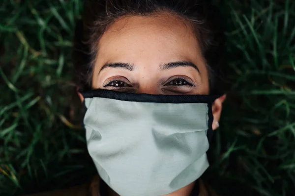 Fénykép egy nő arcát visel egy arc maszk feküdt a fűben — Stock Fotó