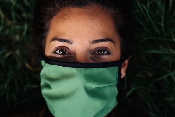 Foto de uma mulher usando uma máscara facial deitada na grama — Fotografia de Stock