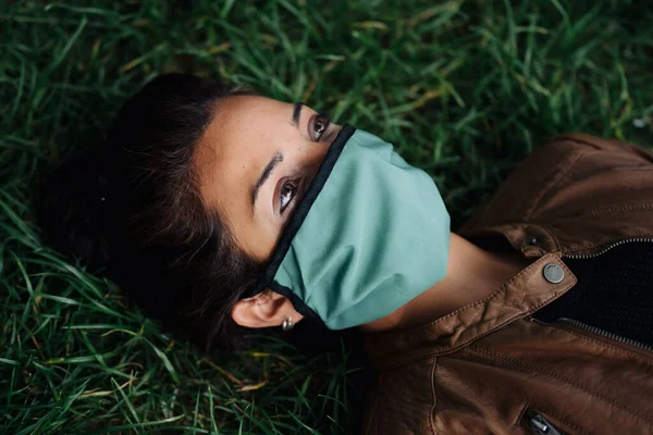 Fénykép egy nőről, aki maszkot visel a fűben fekve — Stock Fotó