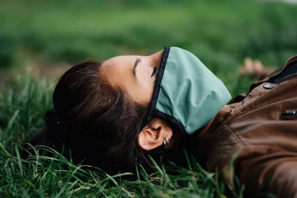 Foto de uma mulher usando uma máscara facial deitada na grama — Fotografia de Stock