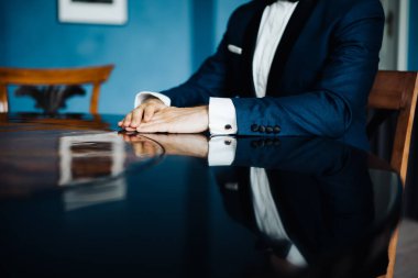 Bir masada sandalyede oturan bir damadın fotoğrafı.
