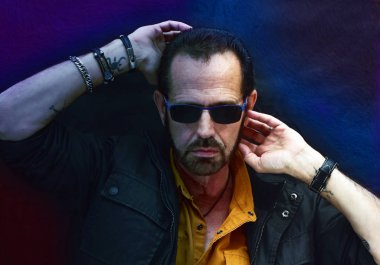 Adam mavi ve dövmeli ışığın altında poz veriyor.