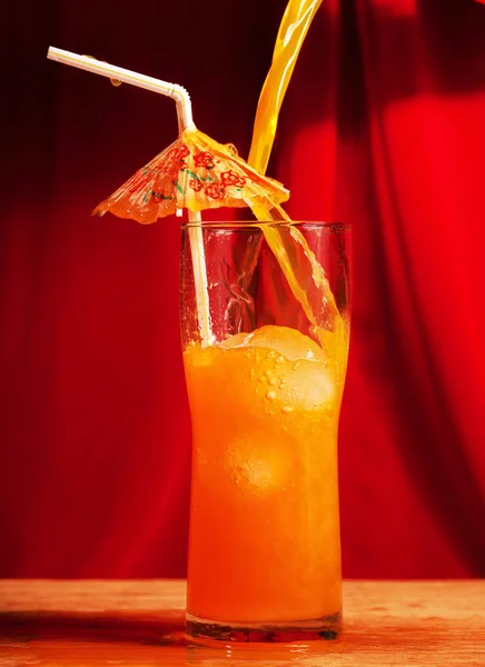 jet pours Orange Drink with ice and umbrella against red background
