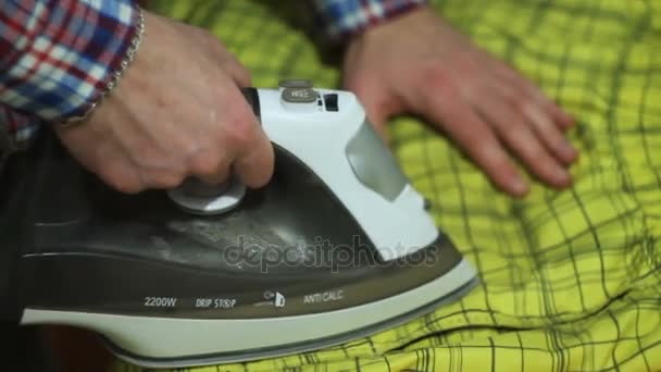 Человек гладит желтые шорты на гладильной доске — стоковое видео