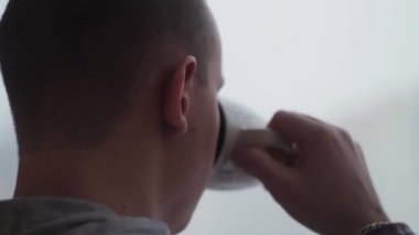 Bunalımlı adam evde, pencerenin kenarında çay içiyor.