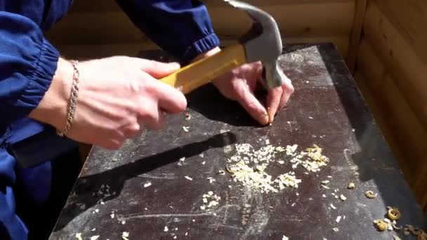 A young worker in the form of strikes with a hammer the nail into the table — Stock Video