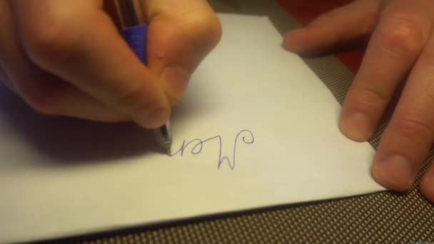 Mann schreibt frohe Weihnachten mit schwarzem Bleistift auf weißem Papier. Ansicht von oben — Stockvideo