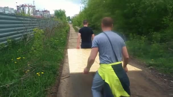 Dos trabajadores llevan una hoja de madera contrachapada. lentitud — Vídeo de stock