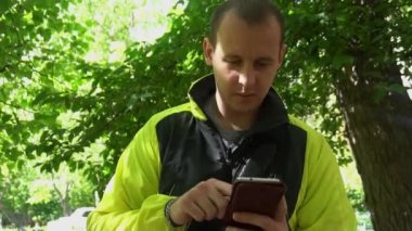 genç adam telefonda, yeşil ağaçlar arka planda çalmaya