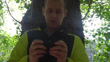 genç adam telefonda, yeşil ağaçlar arka planda çalmaya