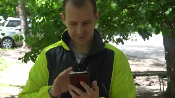 Joven jugando el teléfono, en el fondo de los árboles verdes — Vídeo de stock