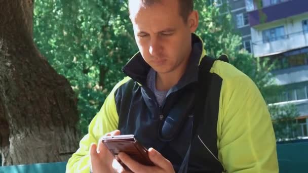 Joven jugando el teléfono, en el fondo de los árboles verdes — Vídeos de Stock