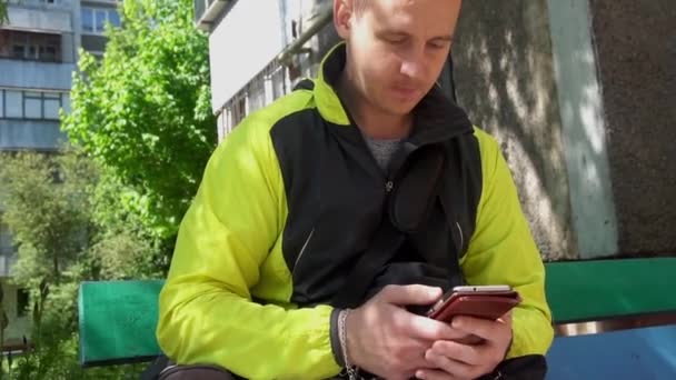 Young man playing the phone, in the background of green trees — стоковое видео